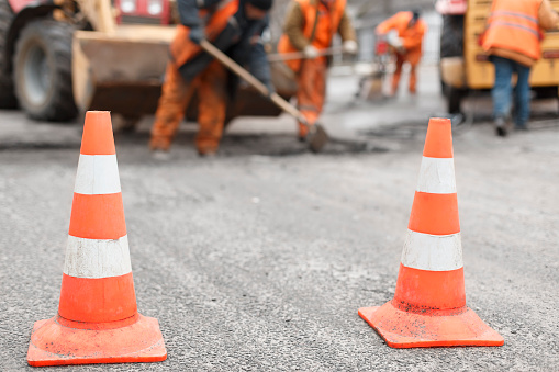 road workers repairing the road with shovels, dub asphalt with shovels at the back, the cones in the foreground